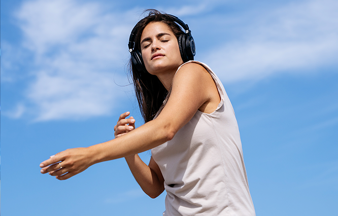 Andrea Lacoste with headphones on, eyes closed, under a blue sky.
