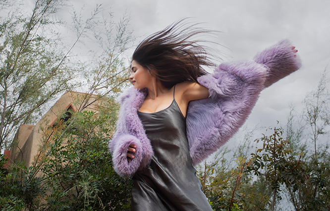 Andrea Lacoste dancing energetically outdoors in a purple furry jacket.